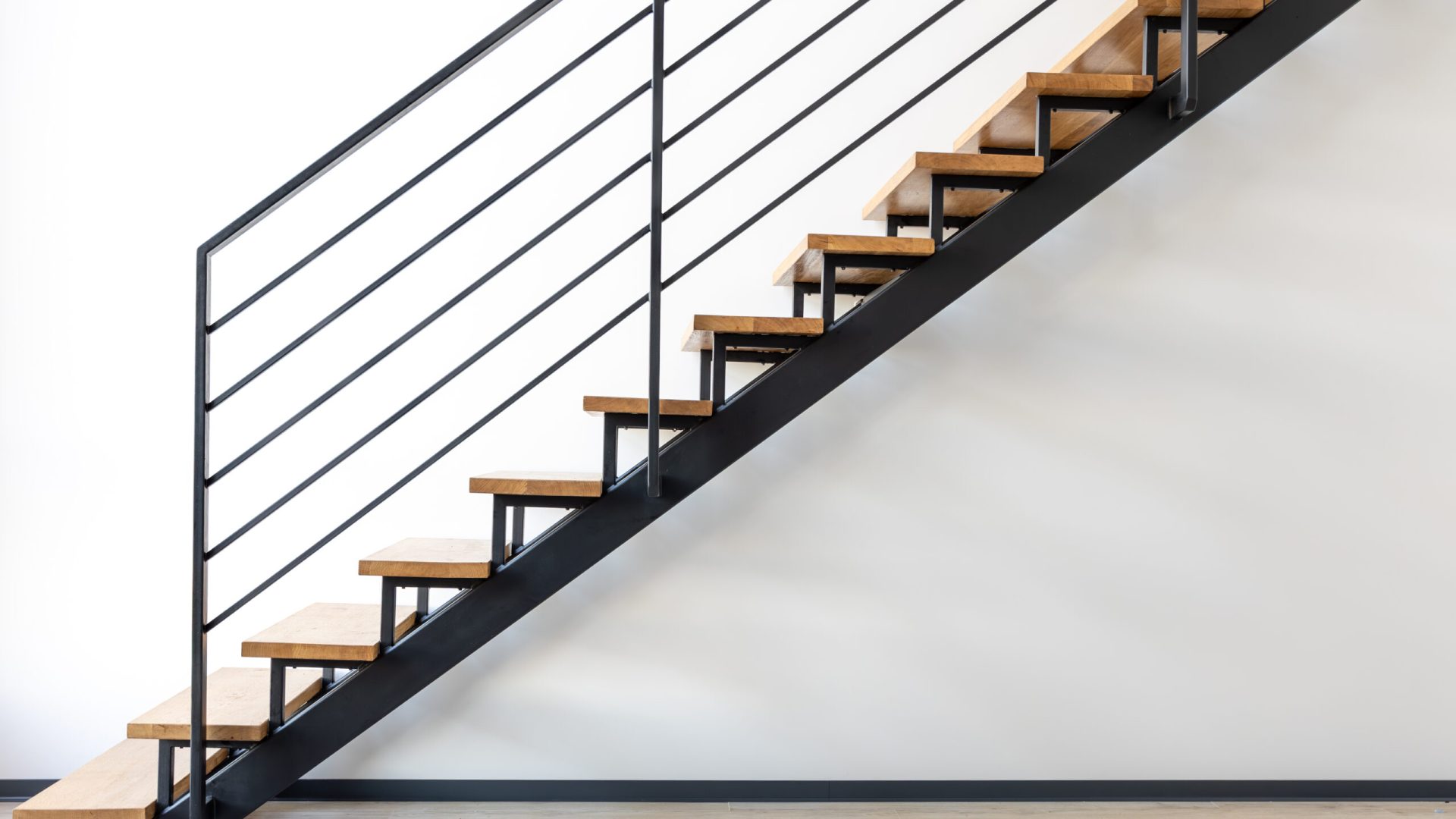 Diagonal view of minimalist metal staircase with natural wood treads against a white wall. Clean industrial design in modern loft apartment. SSUCv3H4sIAAAAAAAAA41PQY6DMAz8i88gEcjSha9UewiJS60CqRKz1Qrl73UoVa+b04wnnhlvQA560K6t6tpW5anp2lKpS1V2Rp/K6tIOONROdTVCAc4wQq+aputUrfX3l9K6klfAYCJZ6DegaVojB8PkF+hFCbg4DDtER+wDmUlYKiCy4TVilDVhVrxHUXf+9jtveS4FJTyuQwap+OfspwAz4mL/sn/KRSY0e9xZpNuDMcxHtudrrpjhPZClZTw6ySl+fuHFc97dE9jbG7lj+XXGlWQachas98kbh+6Q12Em5jcN+Ev4+PxOKT0BOpdm4oQBAAA=